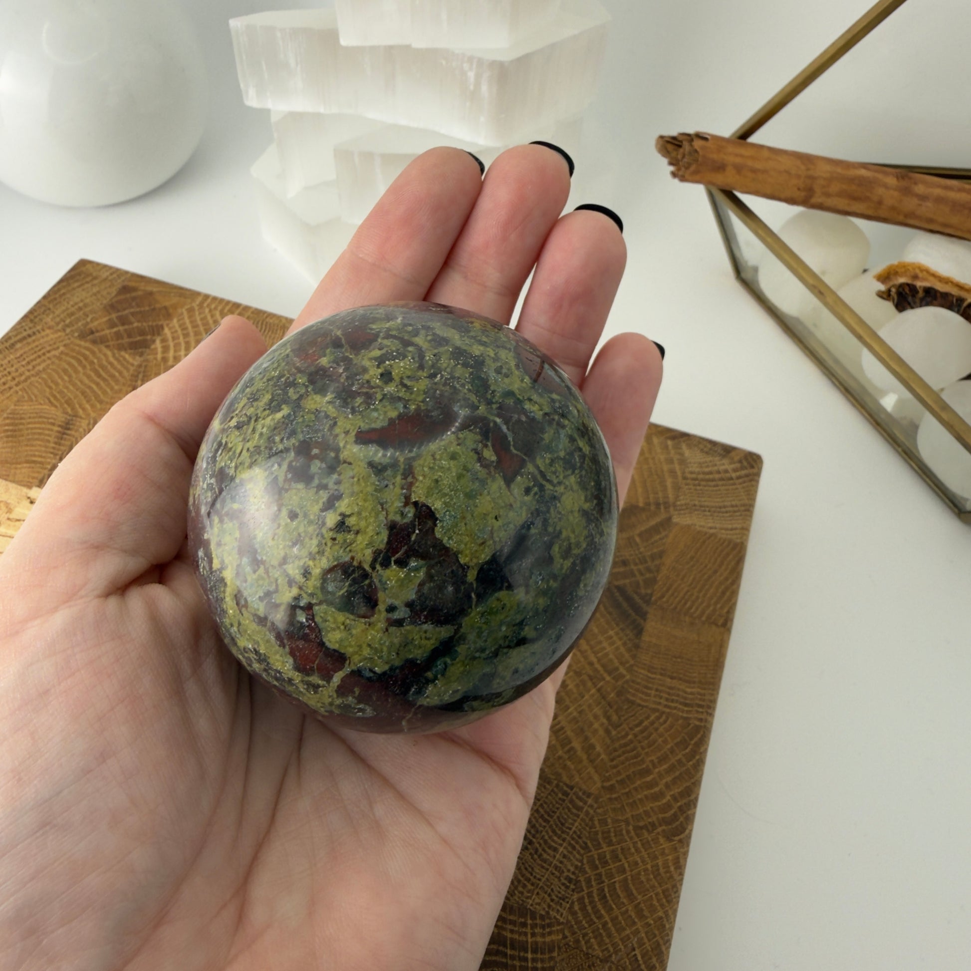 Hand holding a marbled stone sphere with a white surface and wooden objects in the background