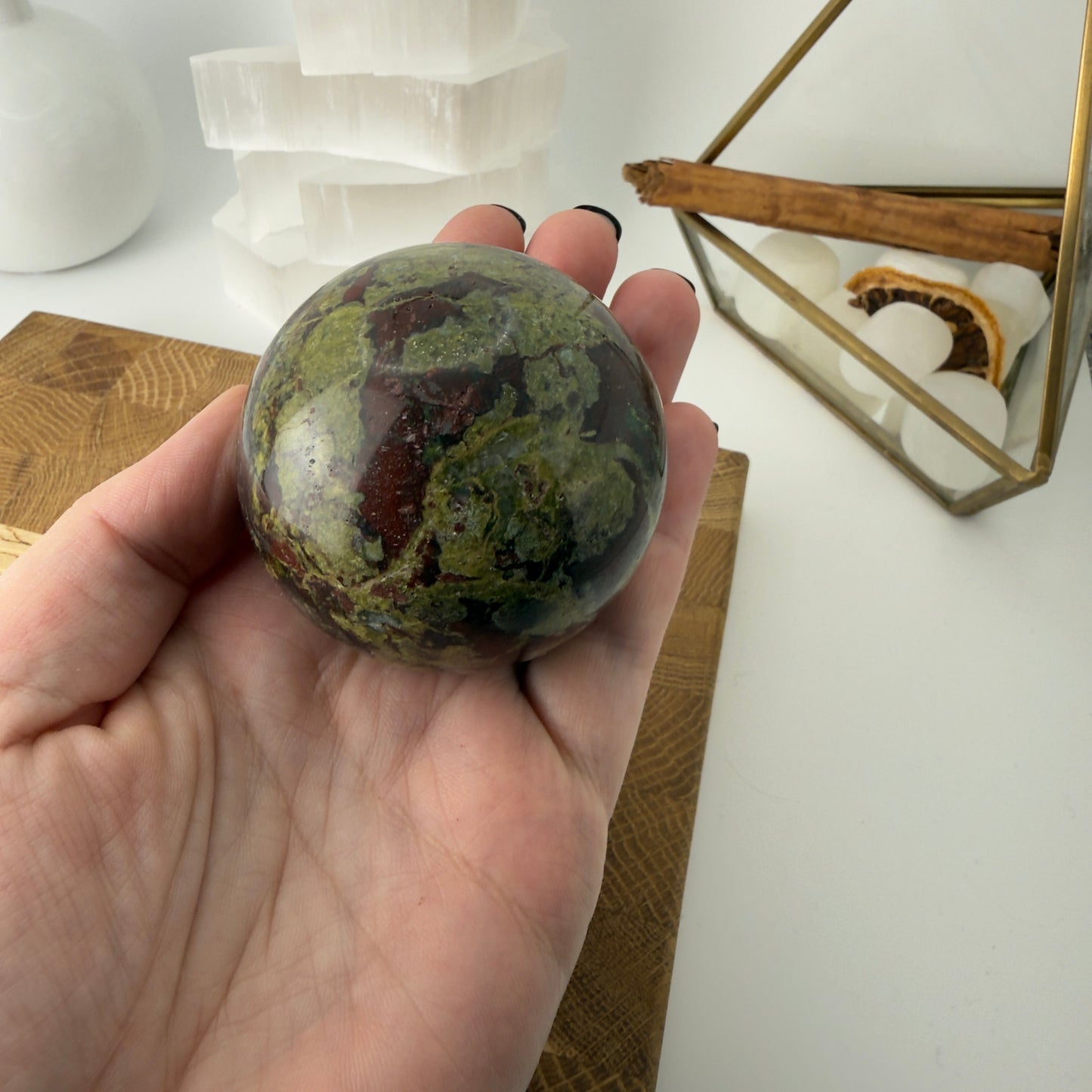 Hand holding a green marbled stone sphere with a white background