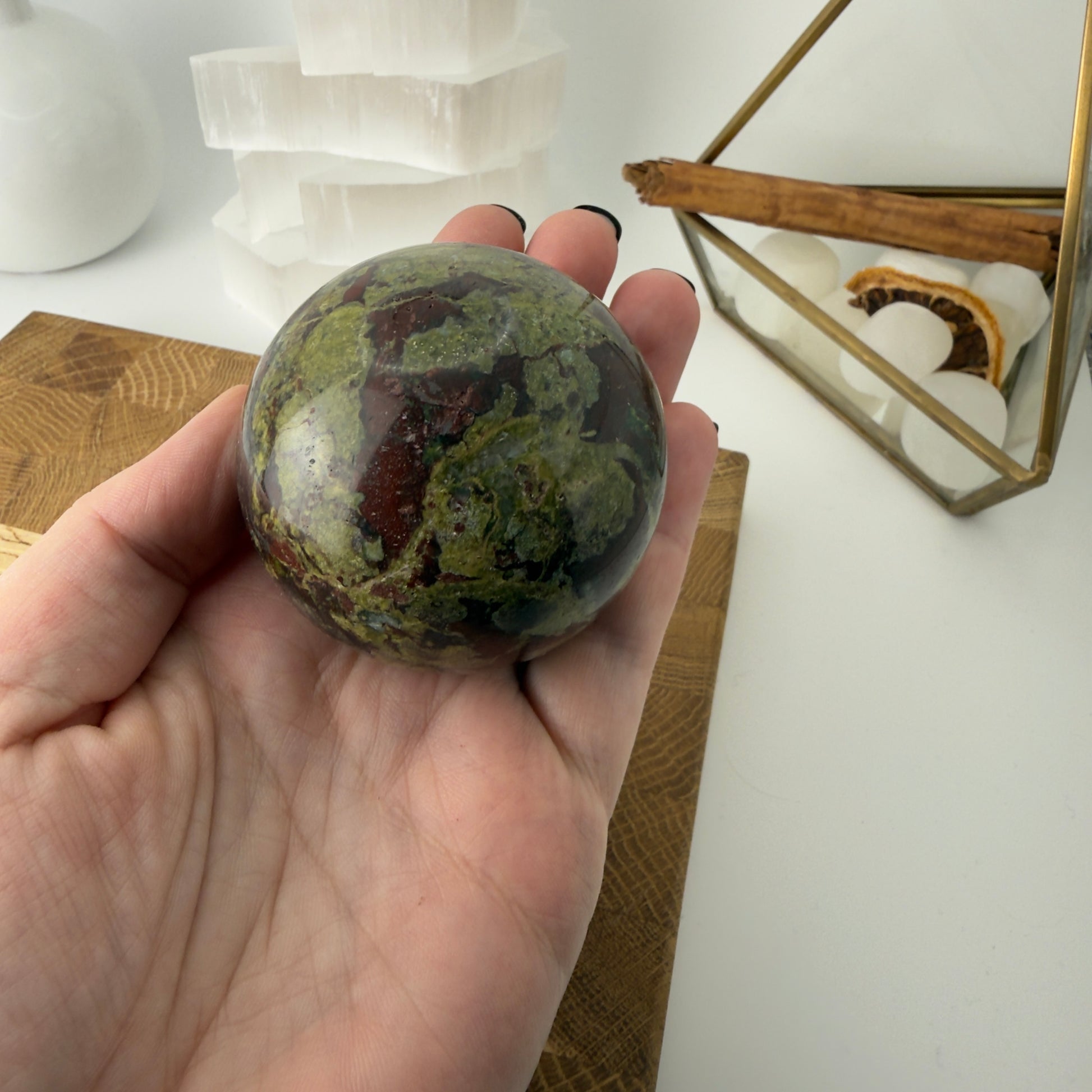 Hand holding a green marbled stone sphere with a white background