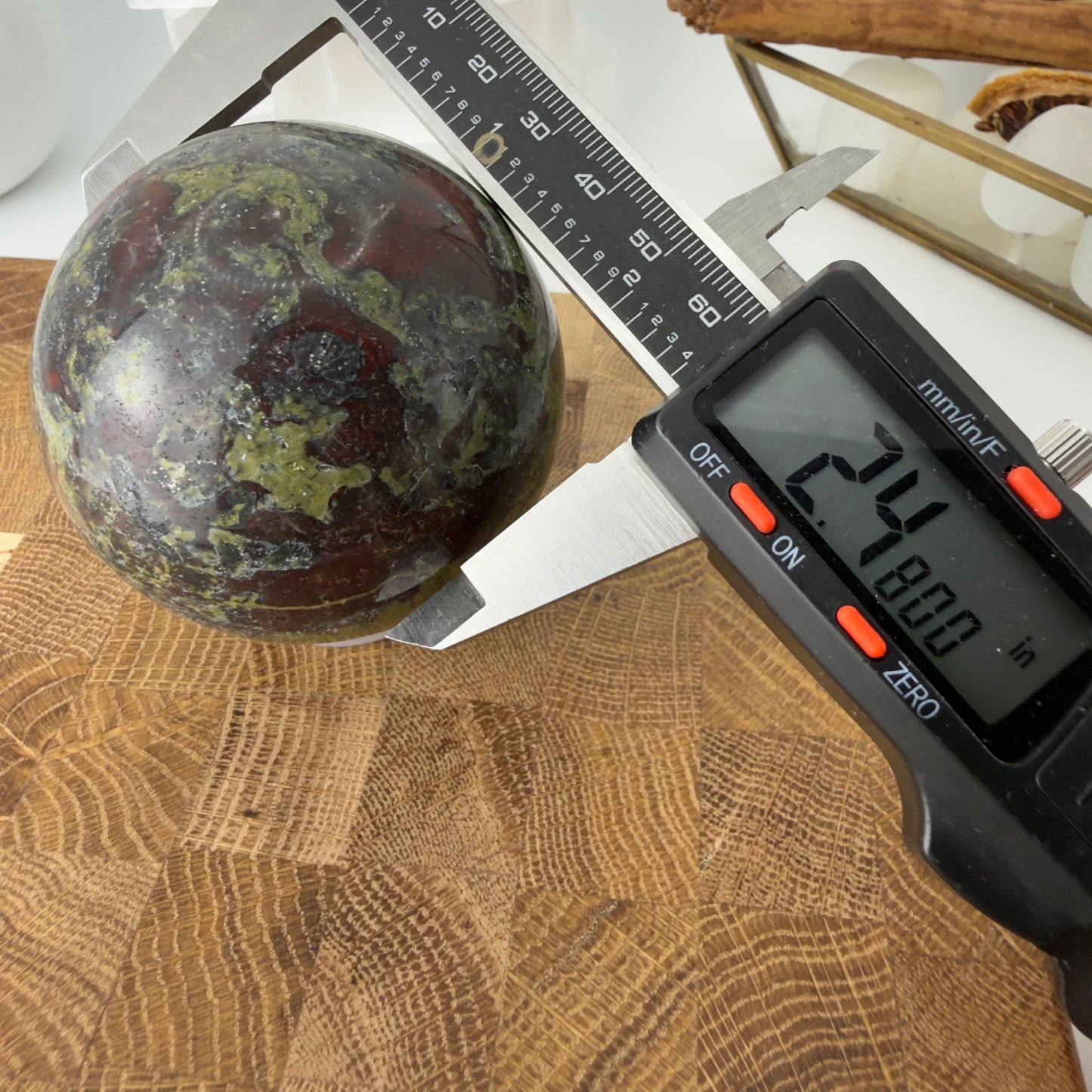 Jasper sphere being measured with a digital caliper on a wooden surface