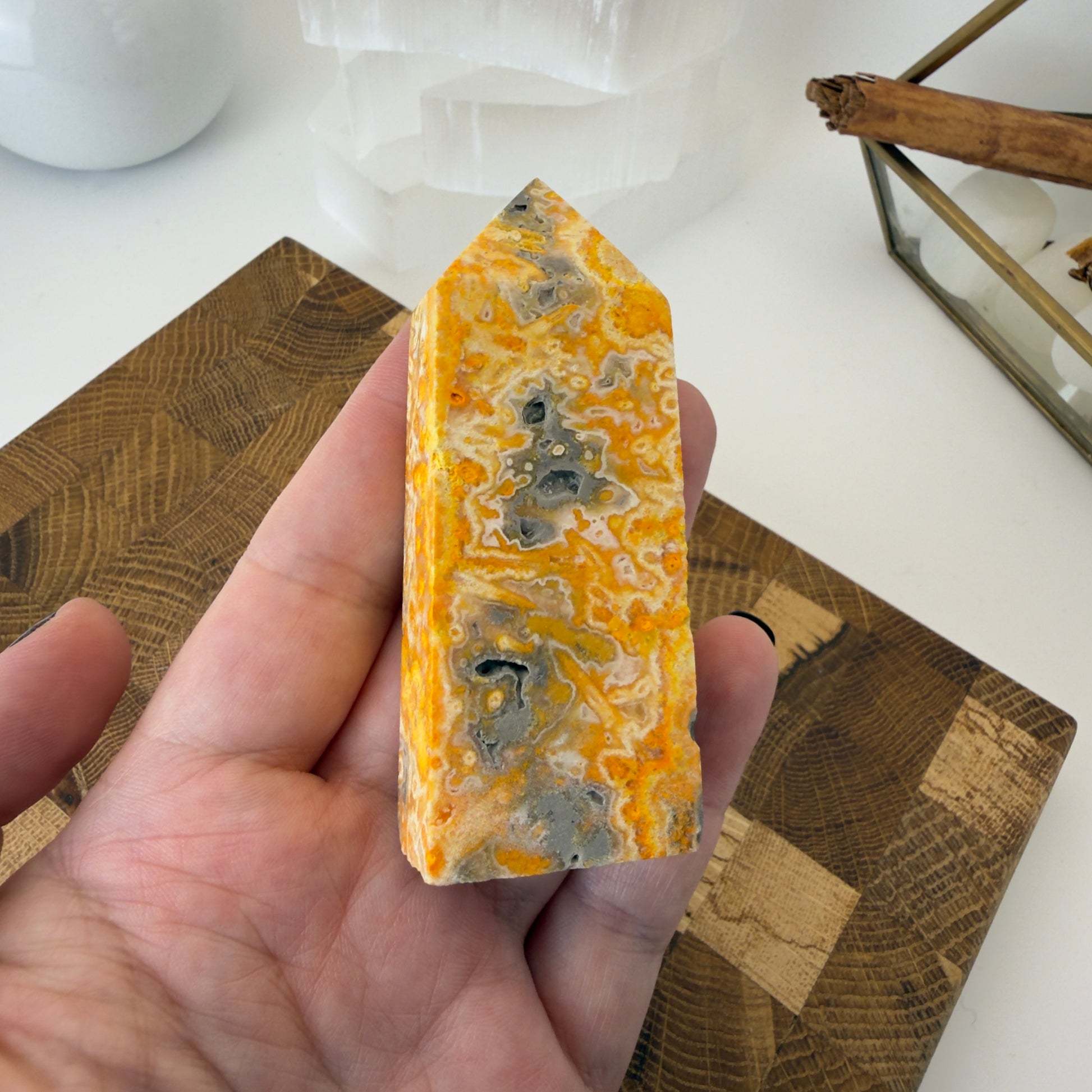 Hand holding a yellow and gray marbled stone with a wooden surface in the background