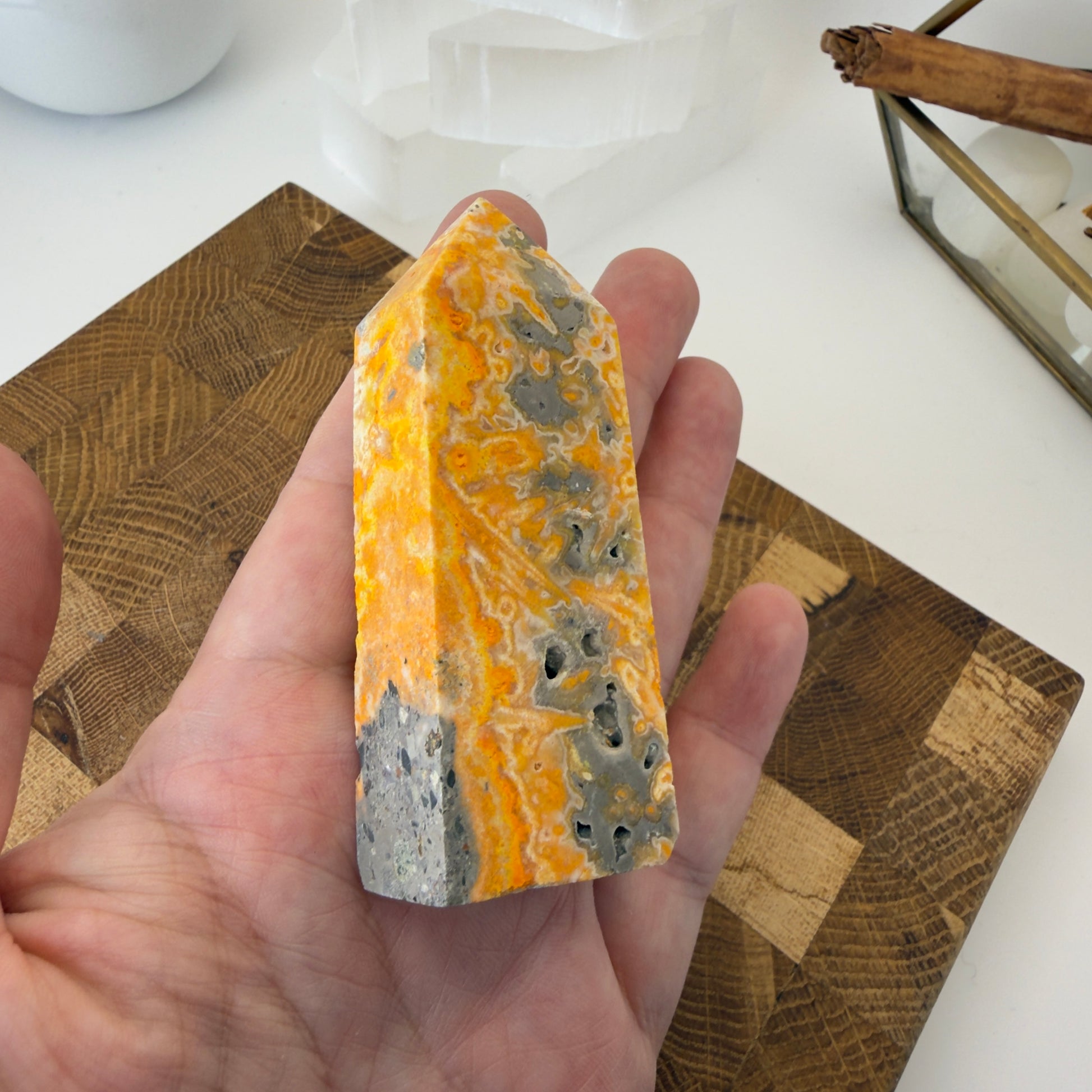 Hand holding a colorful stone with a wooden coaster and cinnamon stick in the background